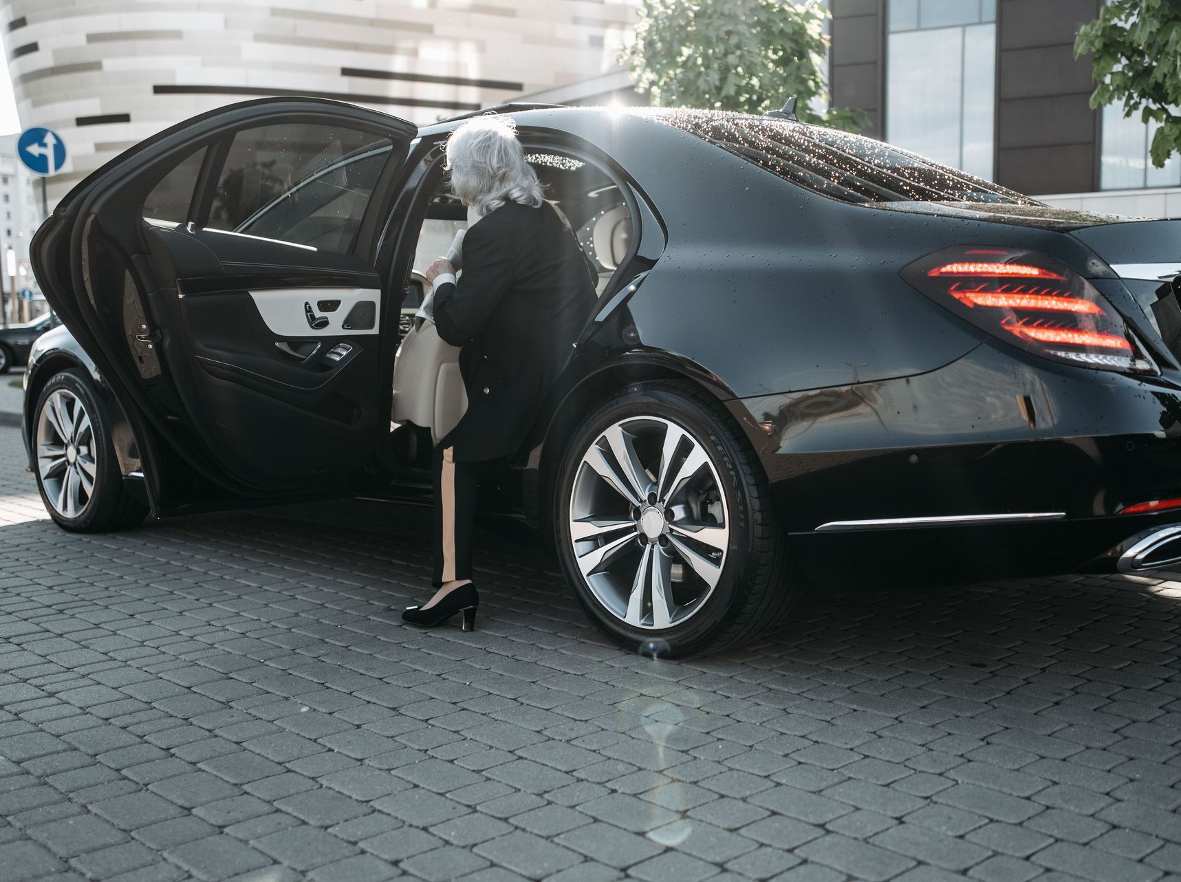 Senior businesswoman stepping out of a sleek black luxury vehicle in a cityscape.